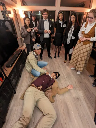 Tiger Oakes lying on the floor, with red X's on his eyes. A crowd is gathered around in shock. Everyone is dressed in 1920s costumes.